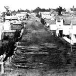 This photo of Bridge Street could have been taken as early as 1878. The upright rectangular outline of the first swing bridge, built that year, is barely visible at the far end. Early Bridge Street, which the Charlevoix Sentinel newspaper called “a horrid spectacle of mud, ruts, and gulches,” does not yet ascend the south hill. It stops where the camera was positioned. To leave Charlevoix in this direction, traffic turned right onto Antrim Street, where the curving wheel tracks are visible, went one block to State Street, turned left up its hill, and left town from there. Bridge Street 1878